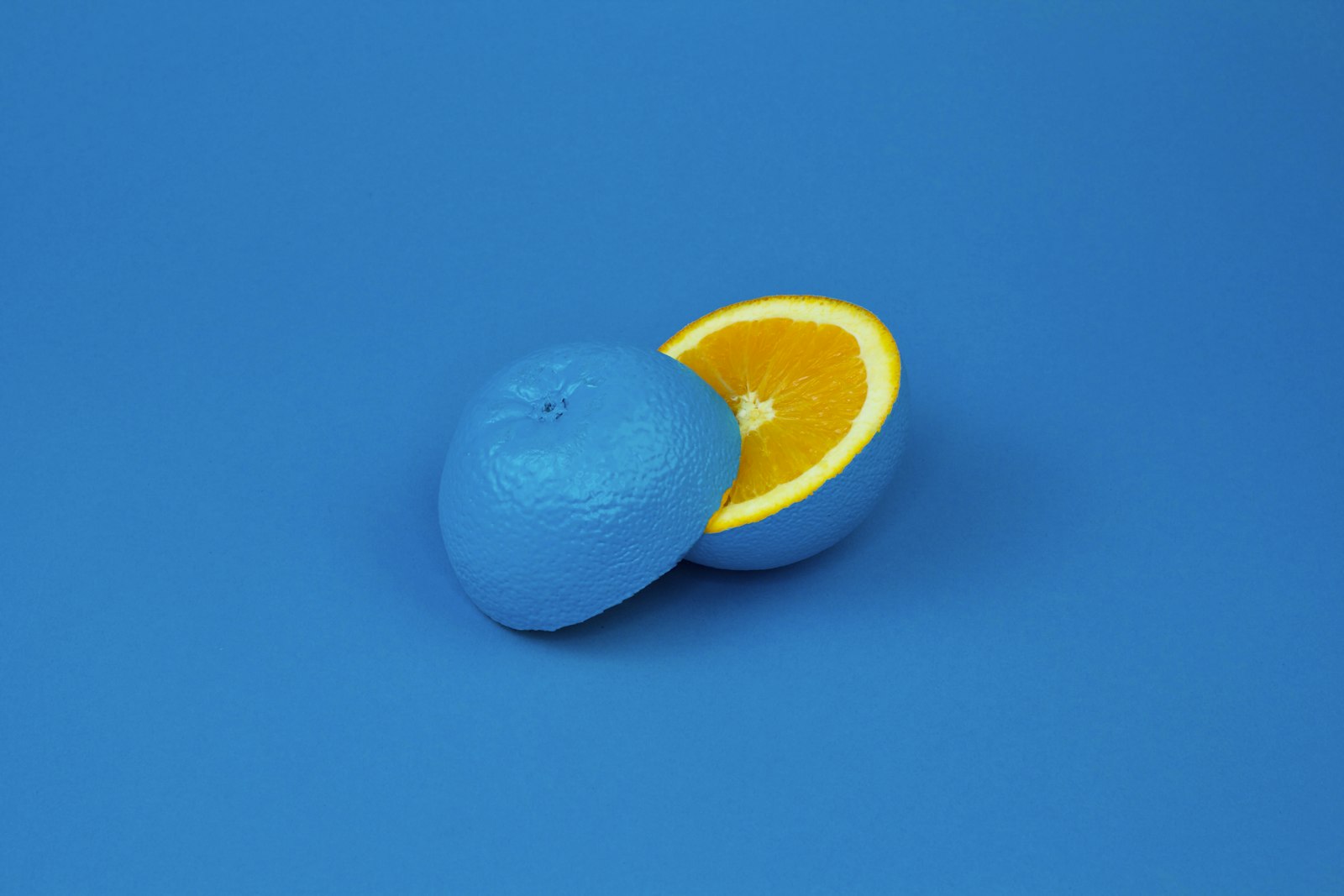 A halved orange with a vibrant blue peel on a matching blue background, revealing its bright orange interior.
